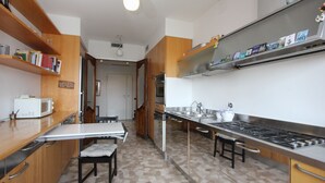 Een keuken met houten kastjes, een wit aanrecht, een magnetron, een fornuis en een eethoek met een tafel en stoelen.