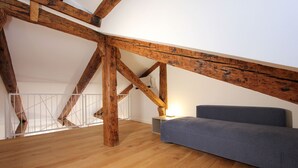 A loft bedroom with exposed wooden beams, a grey sofa, and a staircase with a white railing. - Residence dei 3 Artisti (Venecia)