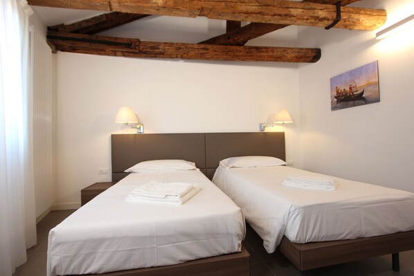 A hotel room with two single beds, wooden headboards, white linens, and two bedside lamps.