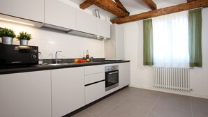 A modern kitchen with white cabinets, a black countertop, a built-in oven, and a window with green curtains. - Residence dei 3 Artisti (Venecia)