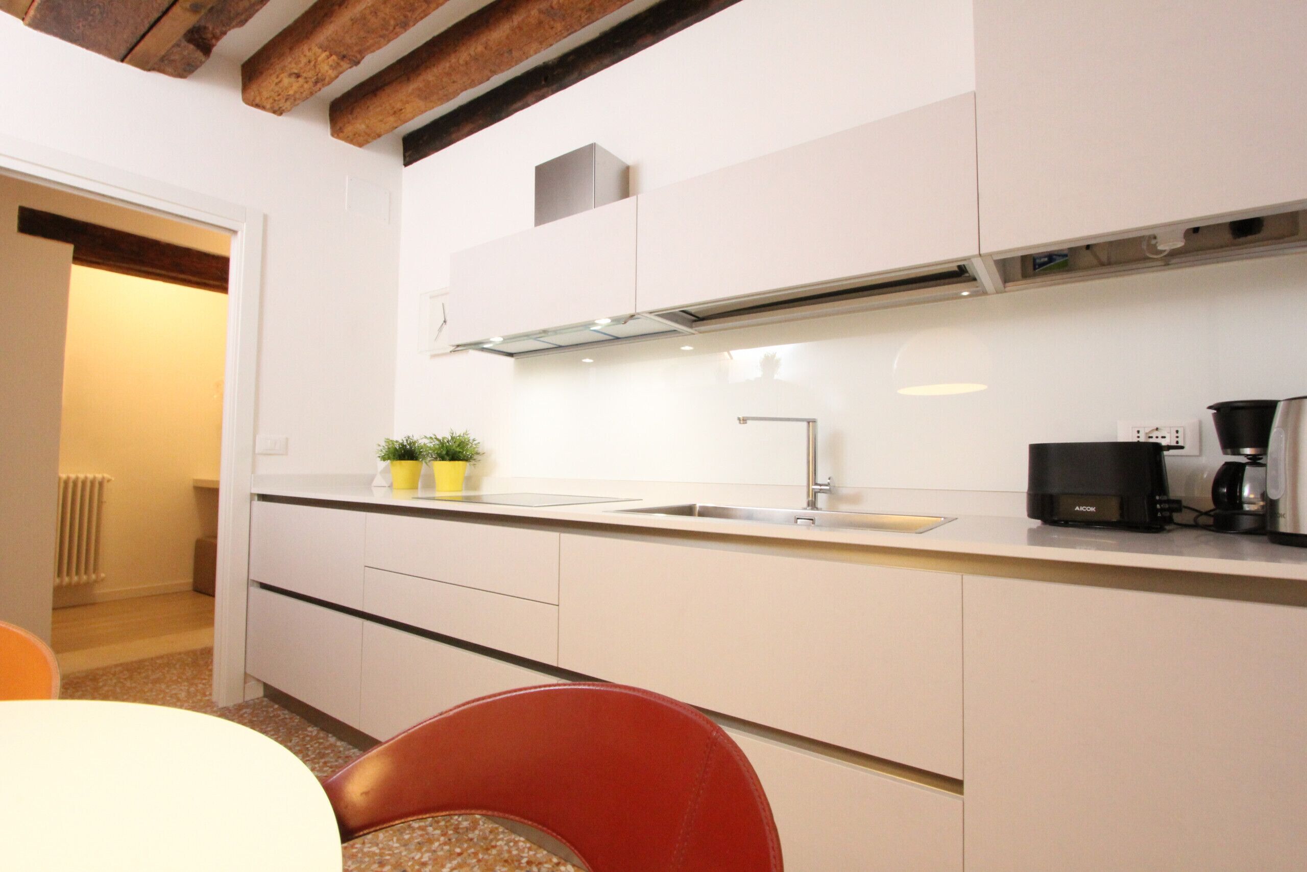 Una cocina moderna con armarios blancos, un lavamanos de acero inoxidable y una máquina de café.