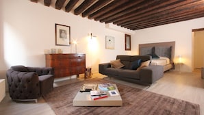 A living room with a fireplace, a sofa, a coffee table with books, and a wooden ceiling. - San Polo Canal View, 500m from Rialto´s Bridge (Venecia)