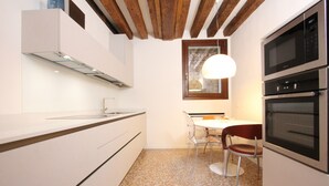 A modern kitchen with white cabinetry, a built-in oven, and a dining area with a table and chairs. - San Polo Canal View, 500m from Rialto´s Bridge (Venecia)