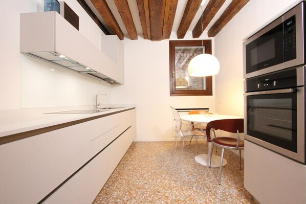 A modern kitchen with white cabinetry, a built-in oven, and a dining area with a table and chairs. - San Polo Canal View, 500m from Rialto´s Bridge (Venecia)