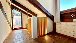 Un couloir étroit avec un plancher en bois, un mur blanc et une poutre en bois au plafond.