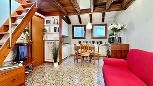 Un salon chaleureux avec un canapé rouge, un escalier en bois, une cuisine, une table à manger et un téléviseur.