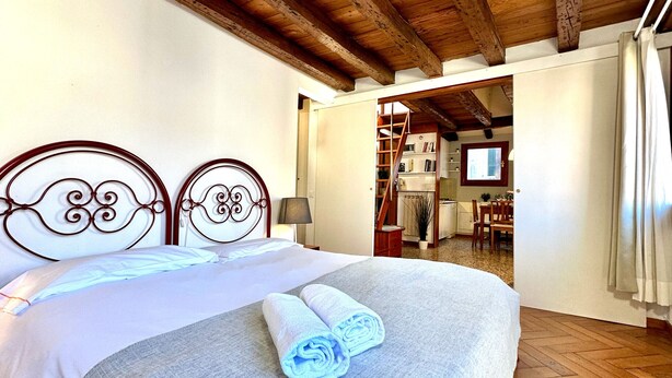 Une chambre avec un grand lit, une tête de lit en bois et une vue sur la cuisine.