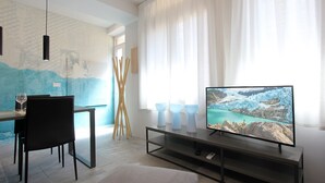 A modern living room with a dining area, a TV on a stand, and a painting on the wall.