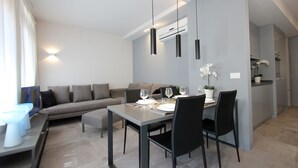 A modern living room with a dining area, grey sofas, a dining table with chairs, and pendant lighting.