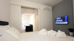 A hotel room with a bed, a TV on the wall, a potted plant, and a stack of towels.