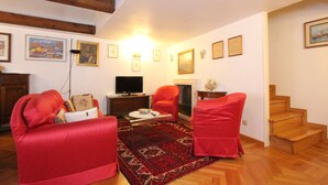Un salon avec un canapé rouge, un téléviseur, une cheminée et un escalier en bois.