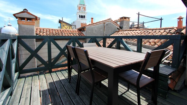 Une terrasse en bois avec une table et des chaises, d’où l’on peut admirer un paysage urbain avec ses bâtiments et son immeuble en hauteur.