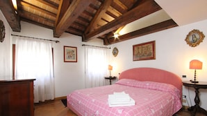Une chambre avec un plafond en bois, un lit avec une literie rose, deux tables de chevet avec des lampes et une commode en bois.