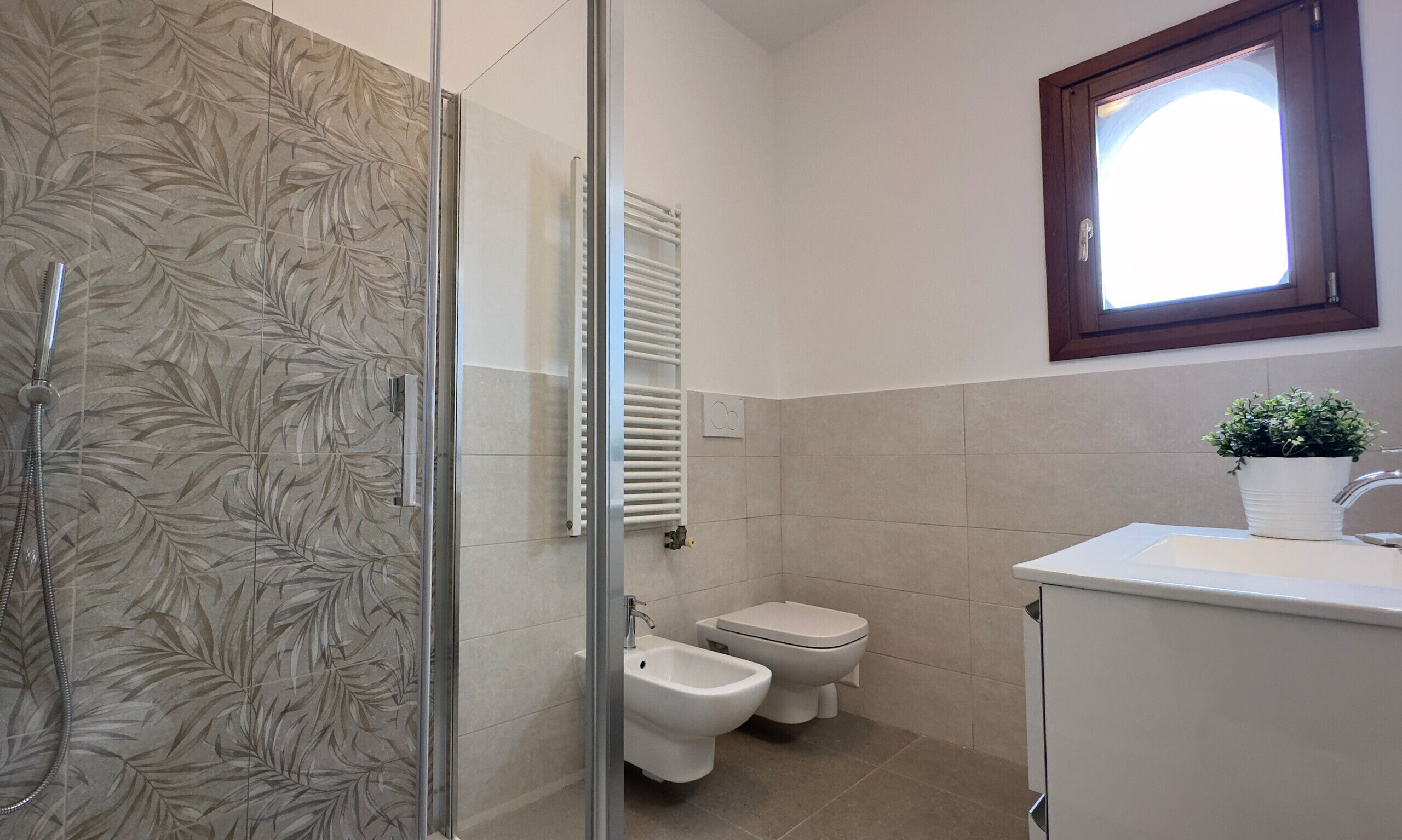 Ein Badezimmer mit Duschkabine aus Glas, einem Bidet, einer Toilette und einem Waschbecken mit Topfpflanze.