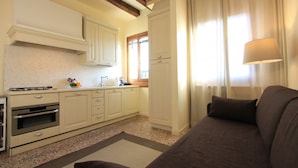 A kitchen with white cabinets, a stove, and a sink. There is a brown sofa in the living area. - Venice Amazing View (St. Mark´s Square 700m) (Venecia)