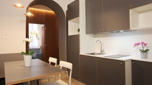 Een moderne keuken met donkere kastjes, een wit aanrecht en een ingebouwde spoelbak. Er staat een eettafel met stoelen en een plant in pot.