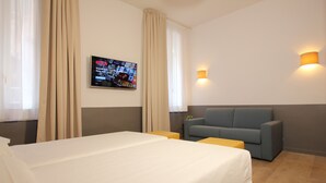 Een hotelkamer met een groot bed, een grijze bank, twee kleine bijzettafeltjes en een aan de muur bevestigde televisie waarop Netflix wordt afgespeeld.
