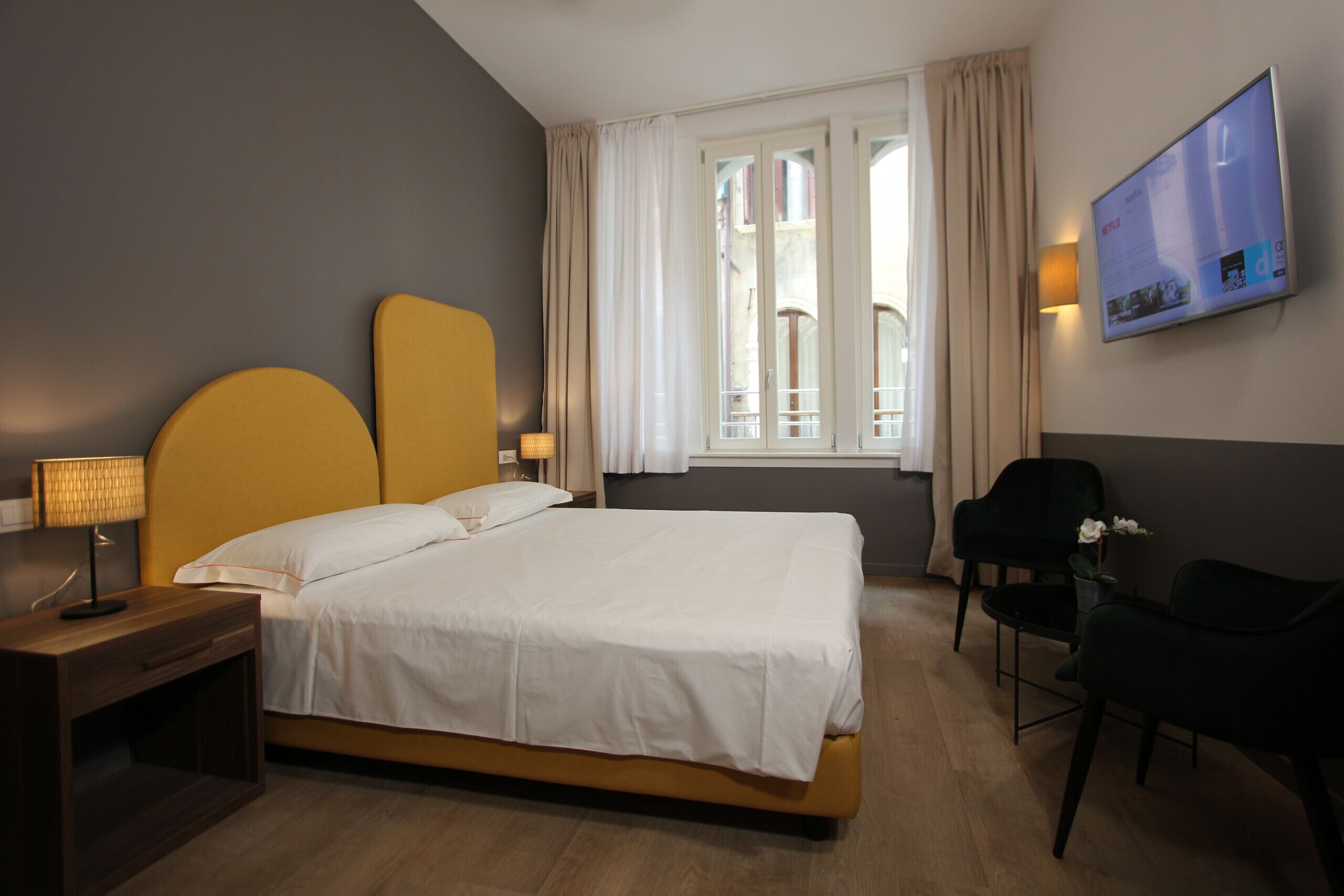 A hotel room with a bed, bedside tables, a TV, and a window with curtains.
