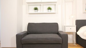 A modern living room with a grey sofa, a white cabinet with two potted plants, and a bedside table with a white pillow. - Rialto Studio (300mt from Rialto´s Bridge) (Venecia)
