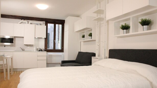 A modern bedroom with a large bed, a desk, and a kitchenette. - Rialto Studio (300mt from Rialto´s Bridge) (Venecia)