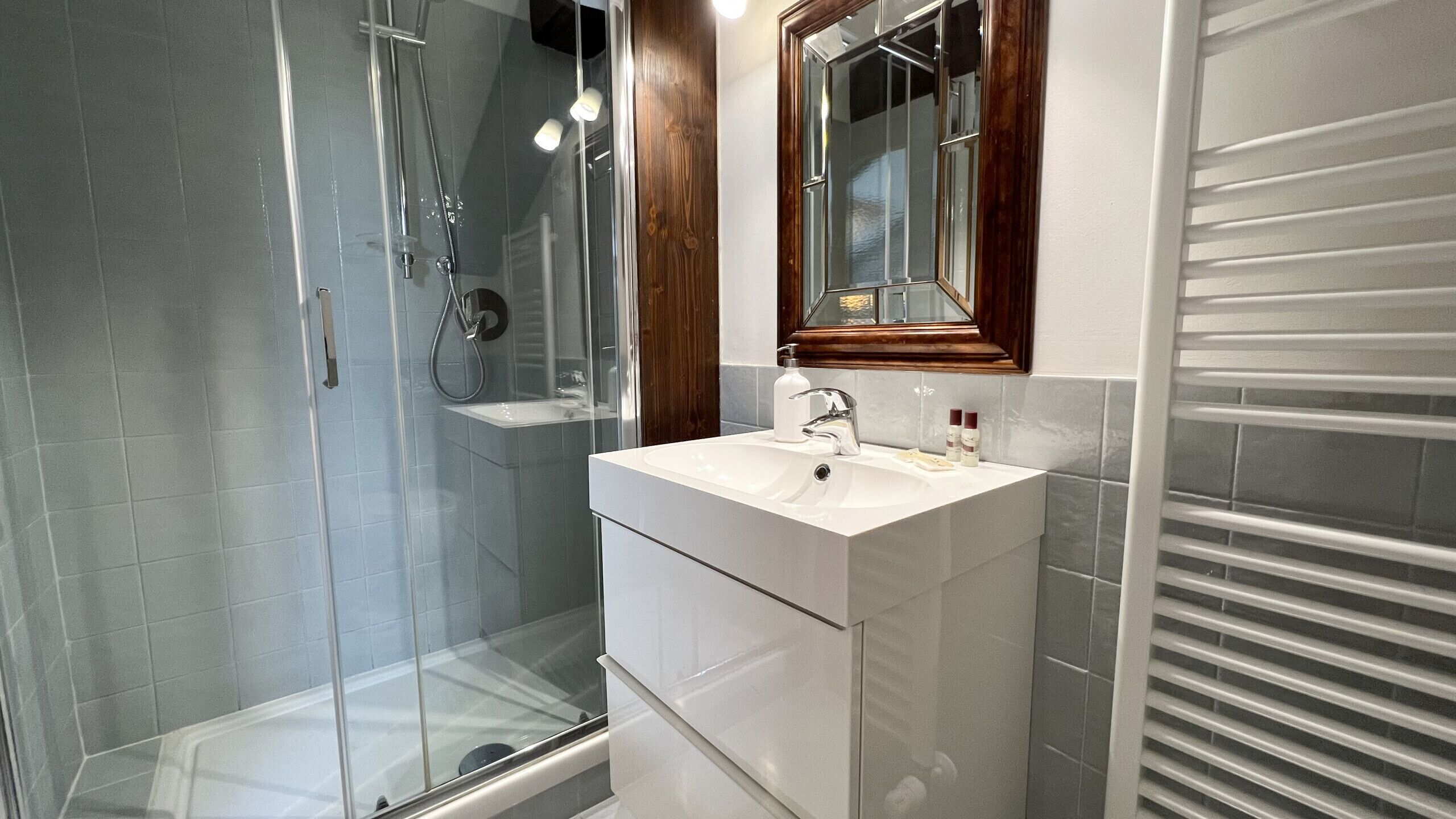 A modern bathroom with a glass-enclosed shower, a white sink with a wooden vanity, and a mirror above the sink.