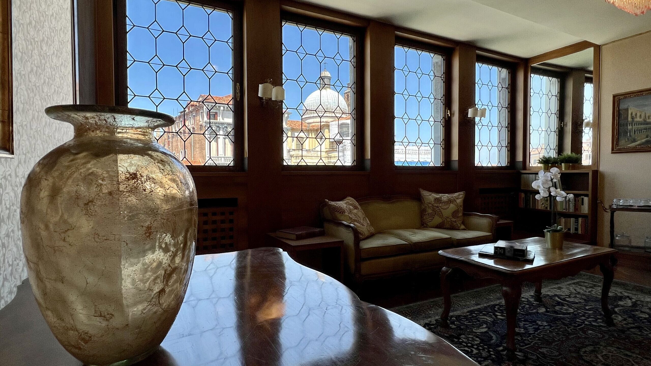 Une pièce avec un grand vase posé sur une table, un canapé et une bibliothèque.