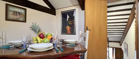 A dining area with a wooden table set for four, fruit on the table, and a painting on the wall.