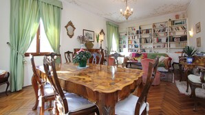 Uma sala de jantar com mesa e cadeiras de madeira, uma estante de livros e um espaço de estar aconchegante com sofá e poltronas.
