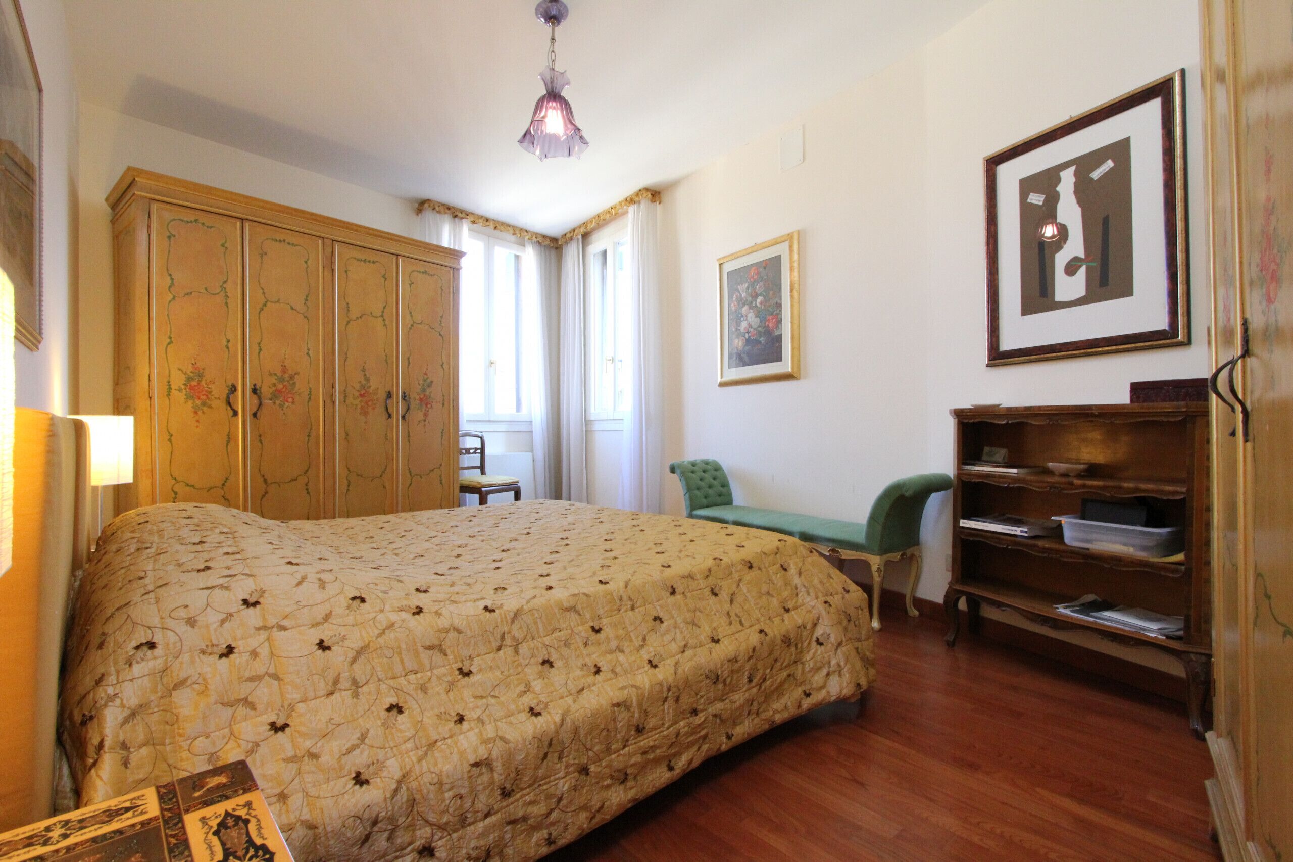 A bedroom with a large bed, a wooden wardrobe, a desk, and a chair.