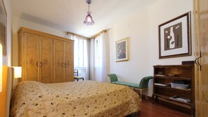 Um quarto com uma cama grande, um guarda-roupa de madeira, uma escrivaninha e uma cadeira.