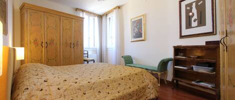A bedroom with a large bed, a wooden wardrobe, a desk, and a chair.