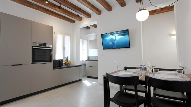 A modern kitchen with built-in appliances, a dining area with a table set for four, and a TV mounted on the wall.