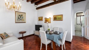 A dining area with a table set for four, white chairs, a chandelier, and framed artwork on the walls.