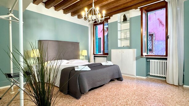 A bedroom with a bed, a chandelier, a radiator, and a window with curtains. - San Marco Canal View (200m from St. Mark´s Square) (Venecia)