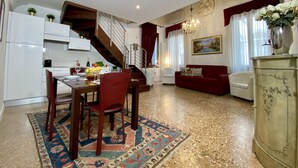 A modern kitchen with white cabinets, a dining area with a table and chairs, a red sofa, and a staircase leading to an upper level. - Manin Terrace (200m from St Mark´s Square) (Venecia)