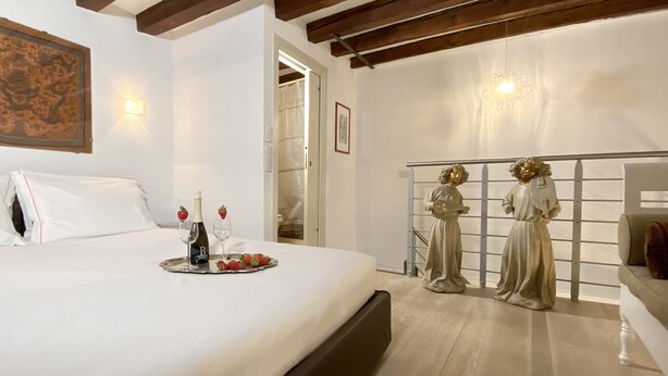 A bedroom with a bed, a bedside table with a bottle and glasses, and two statues on a railing. - Manin Terrace (200m from St Mark´s Square) (Venecia)