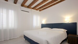 A bedroom with a bed, white curtains, a wooden ceiling, and a nightstand.