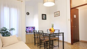 En stue med en sofa, et spisebord med stole, et fjernsyn og en plante.