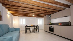 Une cuisine moderne avec un coin repas, caractérisée par un plafond en bois, des armoires blanches et un canapé bleu.