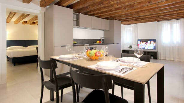 Un espace de repas moderne avec un plafond en bois, une cuisine à l’arrière-plan et un téléviseur sur le côté droit.