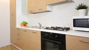 A kitchen with wooden cabinets, a white countertop, a stove, a microwave, and a dishwasher. - San Marco Bis (300 m. from St. Mark´s Square) (Venecia)
