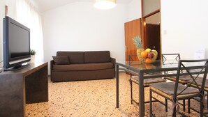 A modern living room with a flat-screen TV, a brown sofa, a glass dining table with chairs, and a fruit bowl on the table. - San Marco Bis (300 m. from St. Mark´s Square) (Venecia)
