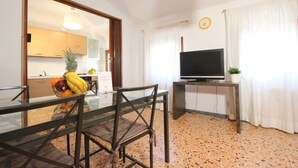 A modern living room with a glass dining table, a dark wooden chair, a television on a wooden stand, and a kitchen visible through an open door. - San Marco Bis (300 m. from St. Mark´s Square) (Venecia)
