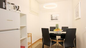 A dining area with a white refrigerator, black chairs, a table with fruit, and a framed picture on the wall. - San Marco Gallery (80m from St Mark´s Square) (Venecia)