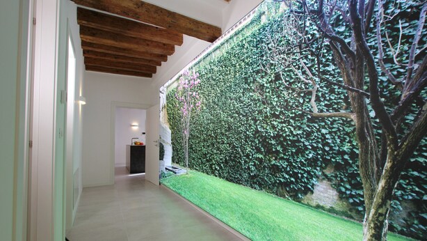 A hallway with a green artificial grass area, a wooden ceiling, and a wall covered with green foliage. - Residence Modern Art 3 (Venecia)