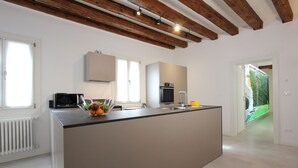 A modern kitchen with a central island, white cabinetry, and a view of a garden through an open door. - Residence Modern Art 3 (Venecia)