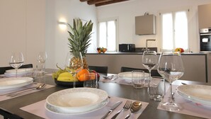 A dining table set with plates, cutlery, and wine glasses, with a fruit bowl and a pineapple on the table. - Residence Modern Art 3 (Venecia)