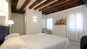 A hotel room with a large bed, a chair, a desk, and a painting on the wall.