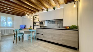 A modern kitchen with a wooden ceiling, a dining area with two chairs, a TV, and a fruit bowl.