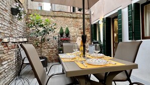 A dining area with a brick wall, a table set for two, and a hanging flower basket. - Acquamarina Terrace (Historical Center) (Venecia)